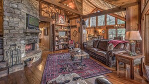 A rustic cabin interior with a stone fireplace, leather sofa, and a large rug. - Winding Log Ridge- Pet Friendly | Screened Porch | 11 miles from Downtown (Blue Ridge)
