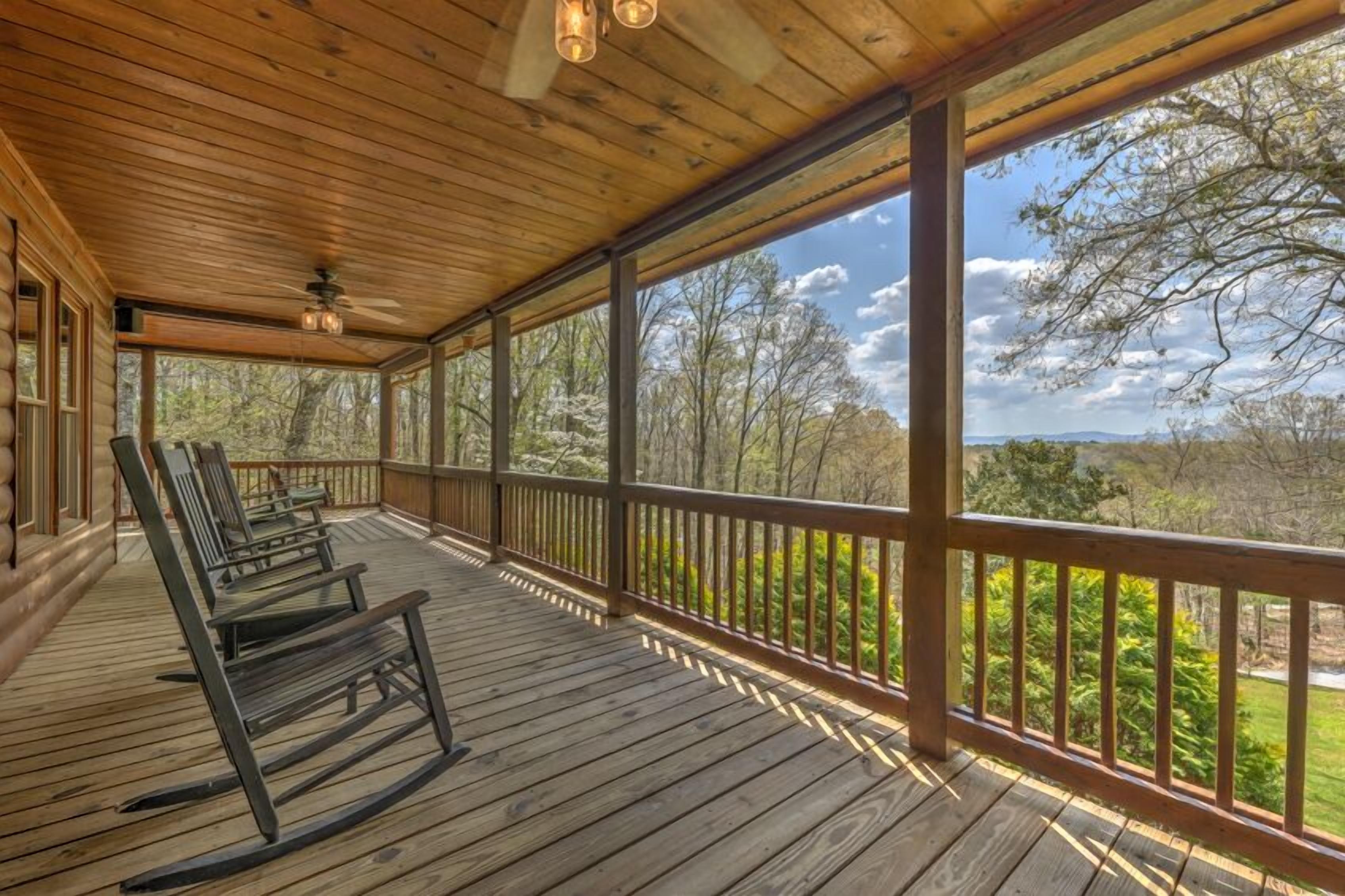 A wooden porch with rocking chairs and a view of trees and hills.