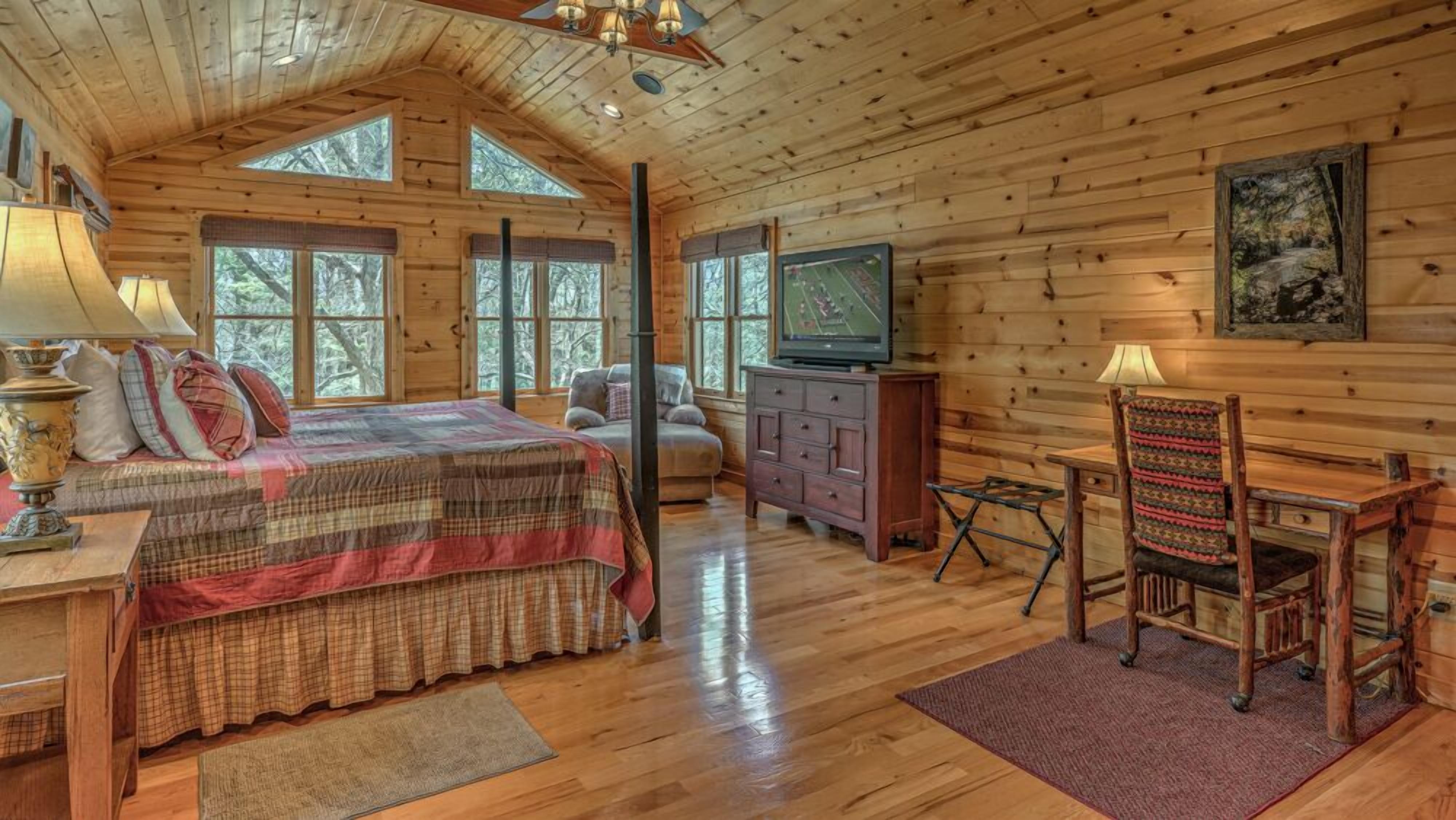 A log cabin bedroom with a bed, dresser, television, and a chair.