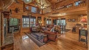 A spacious cabin interior with a large living area, wooden walls, a dining table, and a fireplace. - Tranquility- Pet Friendly | Mountain View | Hot Tub | Pool Table | Shuffleboard | Ping Pong (Mineral Bluff)