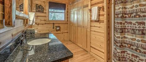 A wooden cabin bathroom with a granite countertop sink, wooden walls, a window, and a shower curtain with animal prints.