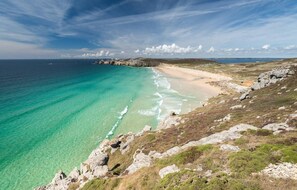 Eine Küstenlandschaft mit klarem türkisblauem Wasser, einem Sandstrand und felsigem Gelände.