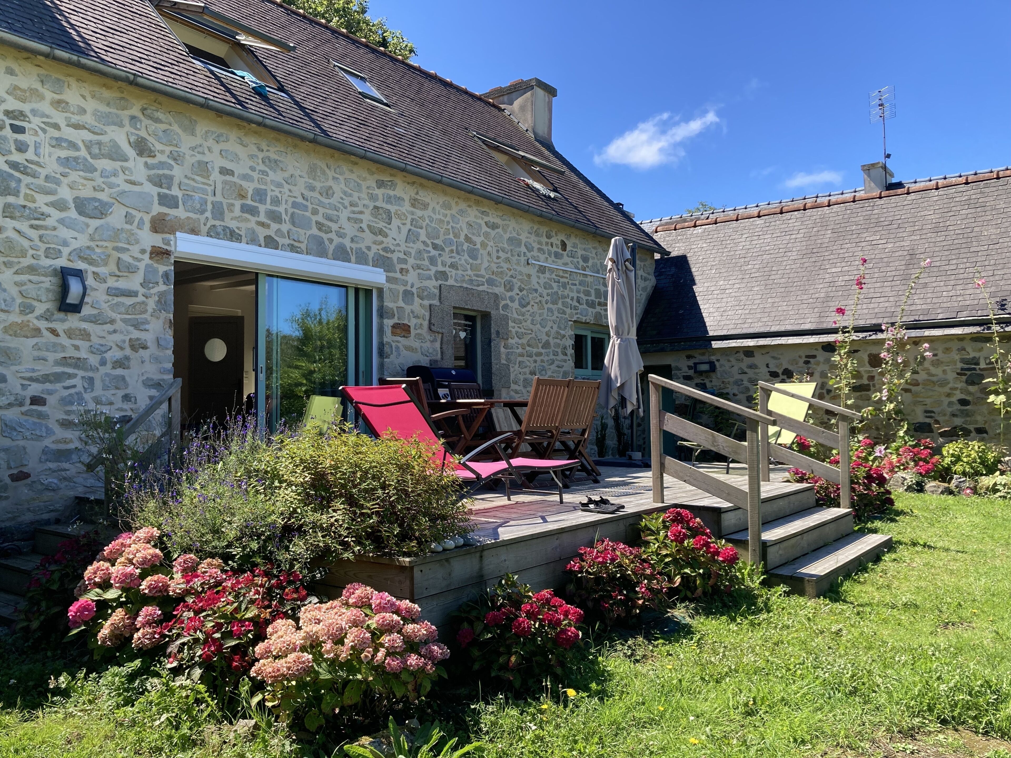 Et stenhus med terrasse, udendørs møbler og en blomsterfuld have.