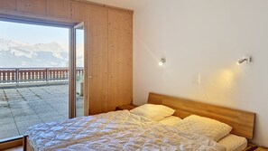 A bedroom with a bed, a wooden headboard, a window with a view of mountains, and two wall-mounted lights. - Hauts de Veysonnaz HV2 001 - SAUNA apartment 8 per (Veysonnaz)