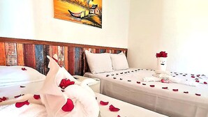 Quarto de hotel com duas camas, um quadro na parede e um vaso com uma rosa na mesa de cabeceira.