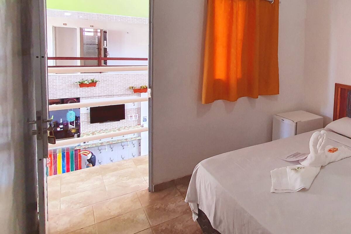 Habitación de hotel con cama, un cuadro, una ventana con cortinas y vista al balcón exterior.