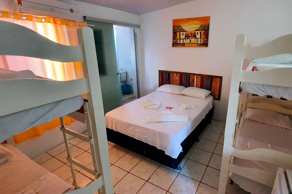 Habitación de hotel con literas, una cama con ropa de cama blanca, un cuadro en la pared y un baño visible a través de una puerta abierta.