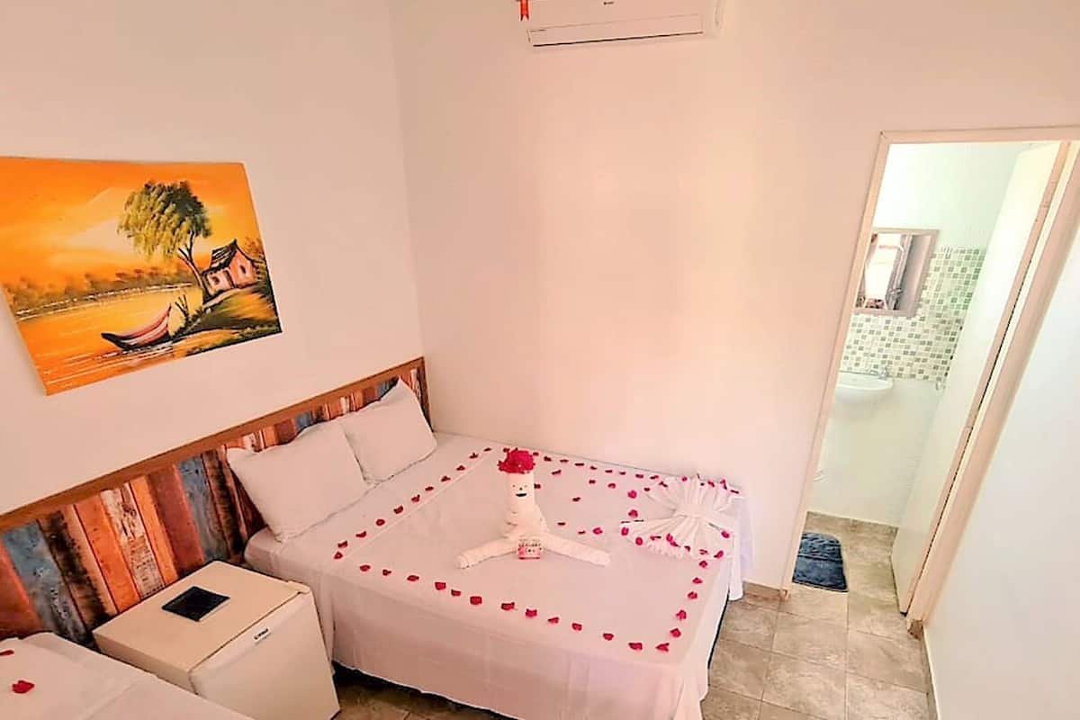 Habitación de hotel con cama, mesita de noche, un cuadro de una escena de atardecer y un baño visible a través de una puerta abierta.