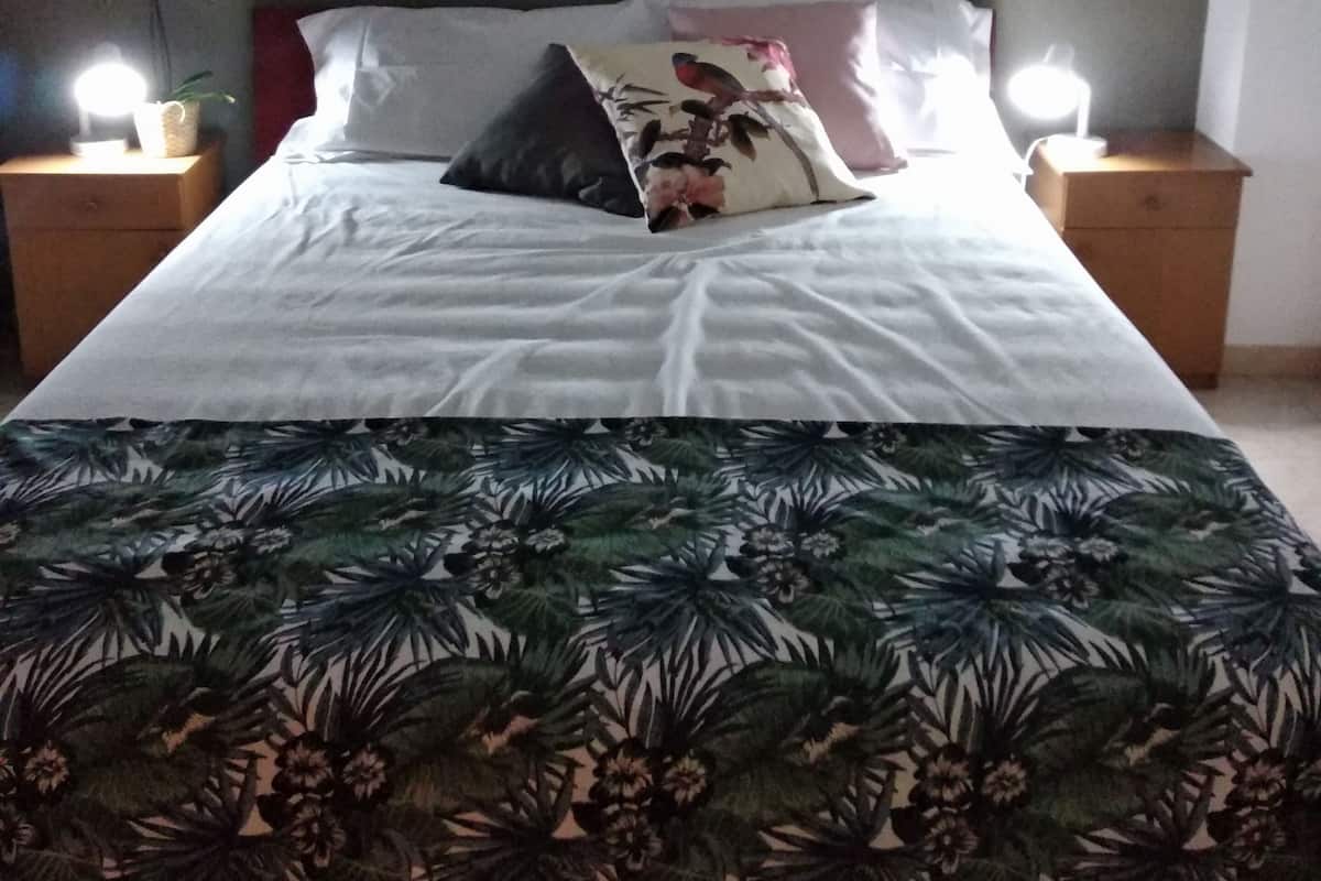 A bed with a floral bedspread, two pillows, and a nightstand with a lamp.