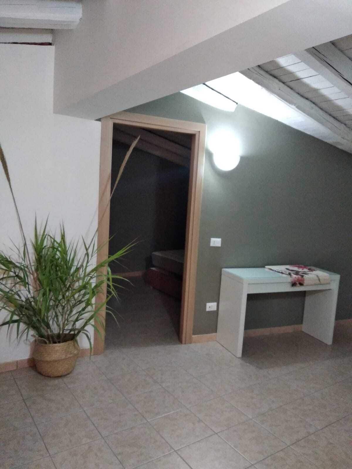 A room with a desk, a potted plant, and a staircase leading to another area.