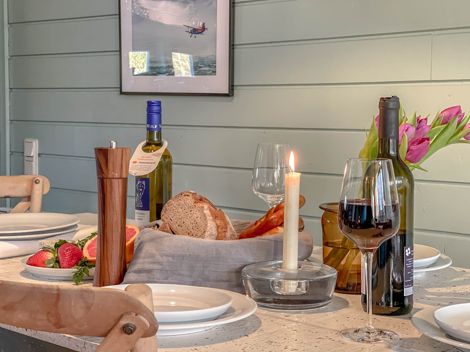 A dining table set with plates, bread, fruit, wine, and a candle.