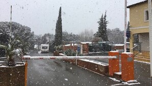 Een besneeuwd landschap met een hek, een geparkeerd voertuig en een gebouw met een gele gevel.