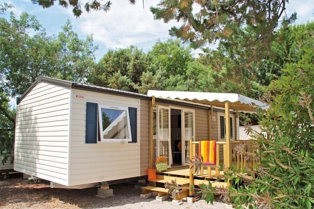 Une maison mobile dotée d’un porche couvert, d’une porte coulissante et d’un petit espace extérieur aménagé pour s’asseoir.