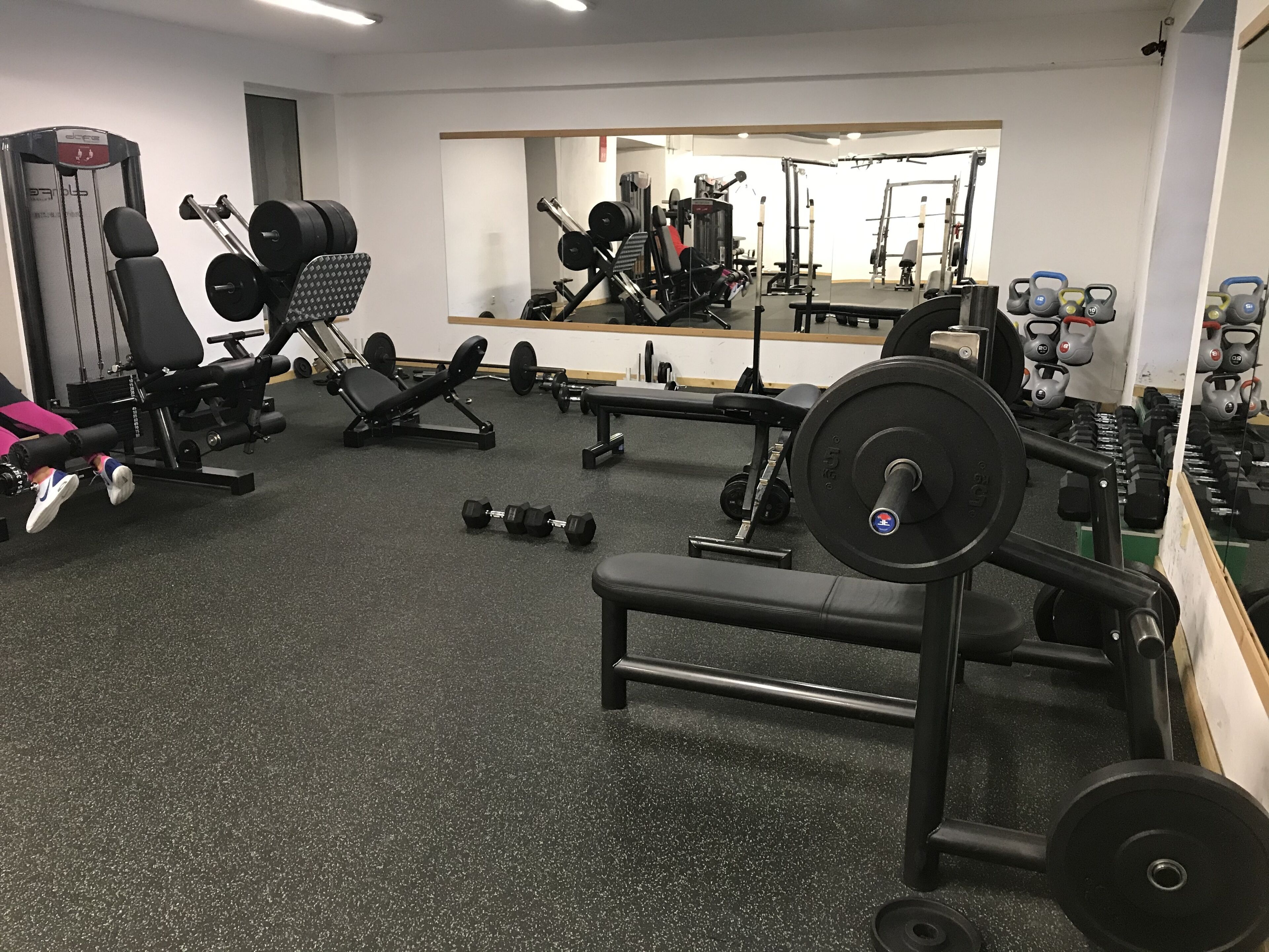 Uma academia com diversos equipamentos de exercícios, incluindo halteres, bancos e aparelhos de musculação.