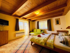 A cozy room with a bed, a green sofa, a television, and a window with curtains. - Penzion Pazicky (Stara Lesna)