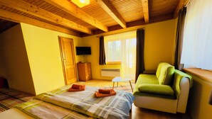 A room with a bed, a green sofa, a TV, a window with curtains, and wooden beams on the ceiling. - Penzion Pazicky (Stara Lesna)