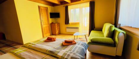 Ein Zimmer mit einem Bett, einem grünen Sofa, einem Fernseher, einem Fenster mit Vorhängen und Holzbalken an der Decke.