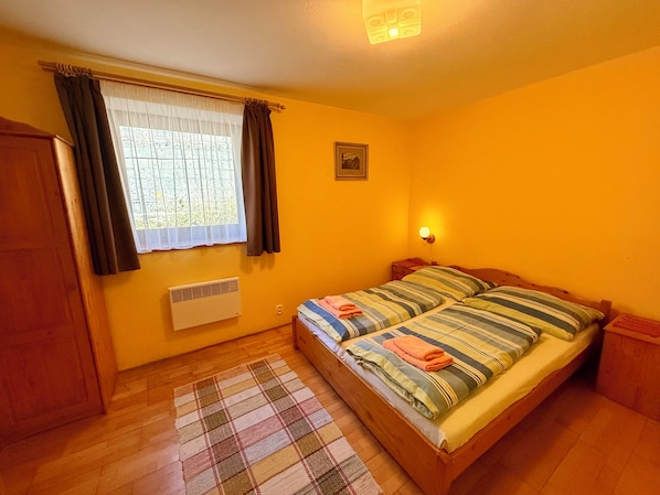 Quarto com cama, janela com cortinas, radiador, luminária na parede e uma pequena imagem.