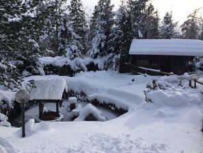 A snow-covered outdoor area with a wooden bench and a lamp post, surrounded by snow-laden trees and a cabin. - Penzion Pazicky (Stara Lesna)