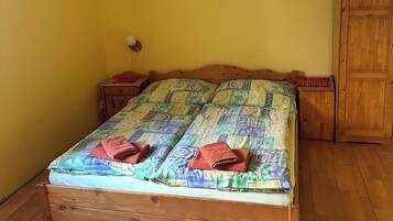 A bedroom with a wooden bed, a wooden wardrobe, a small bedside table, and a wall-mounted lamp.