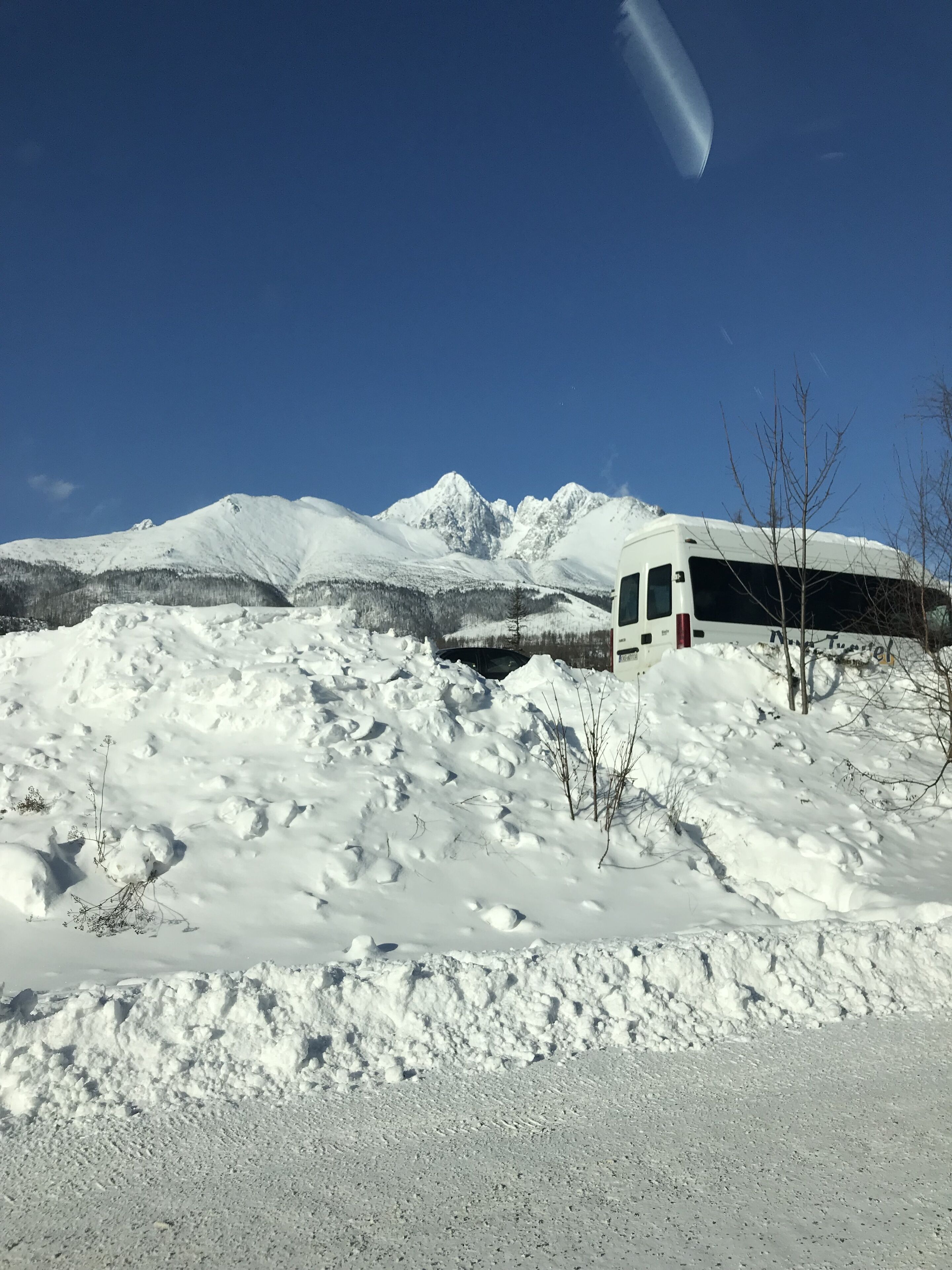Een besneeuwd landschap met een witte camper op een helling, omringd door sneeuw en bomen.