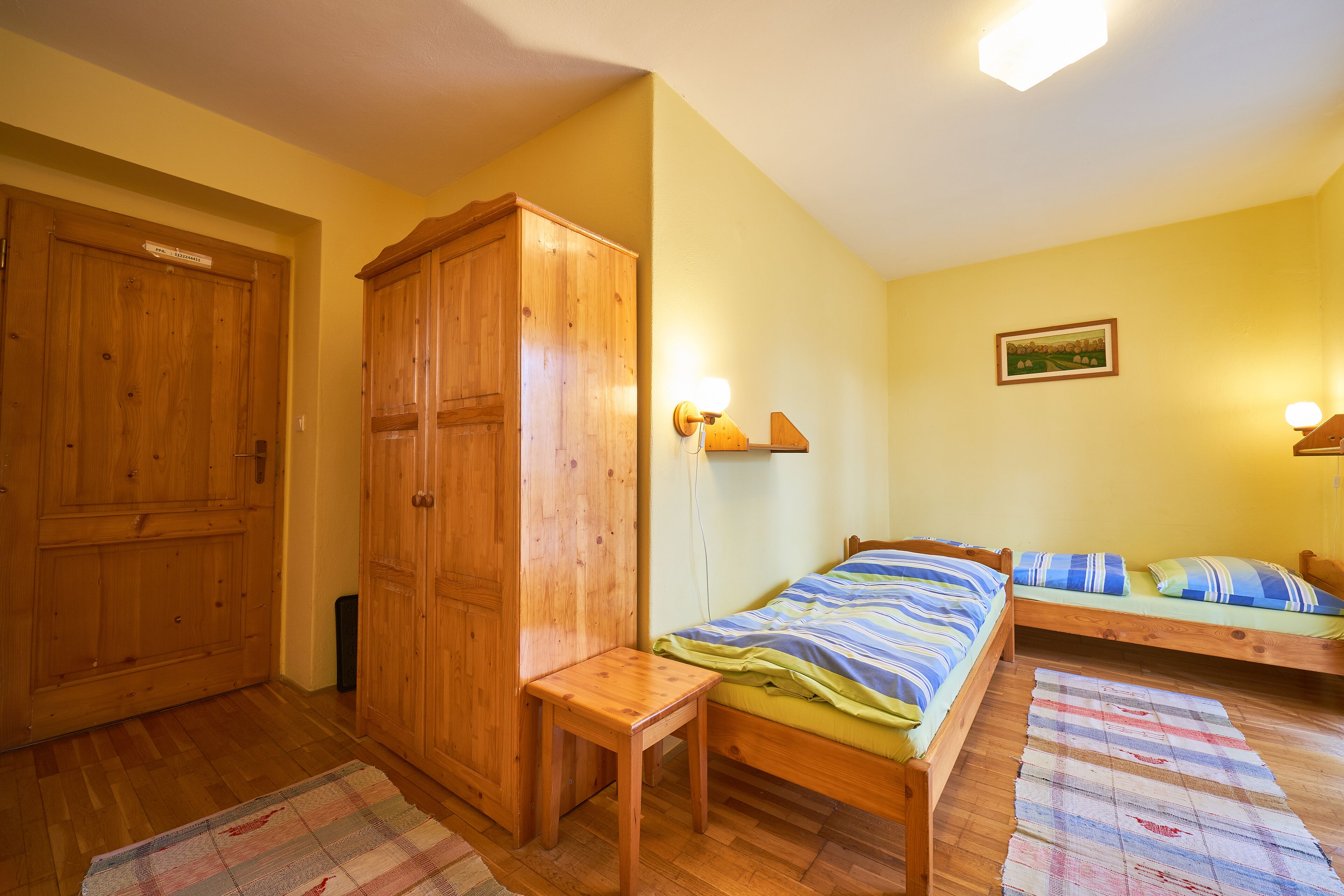 A room with two wooden beds, a wooden wardrobe, and a small wooden table.
