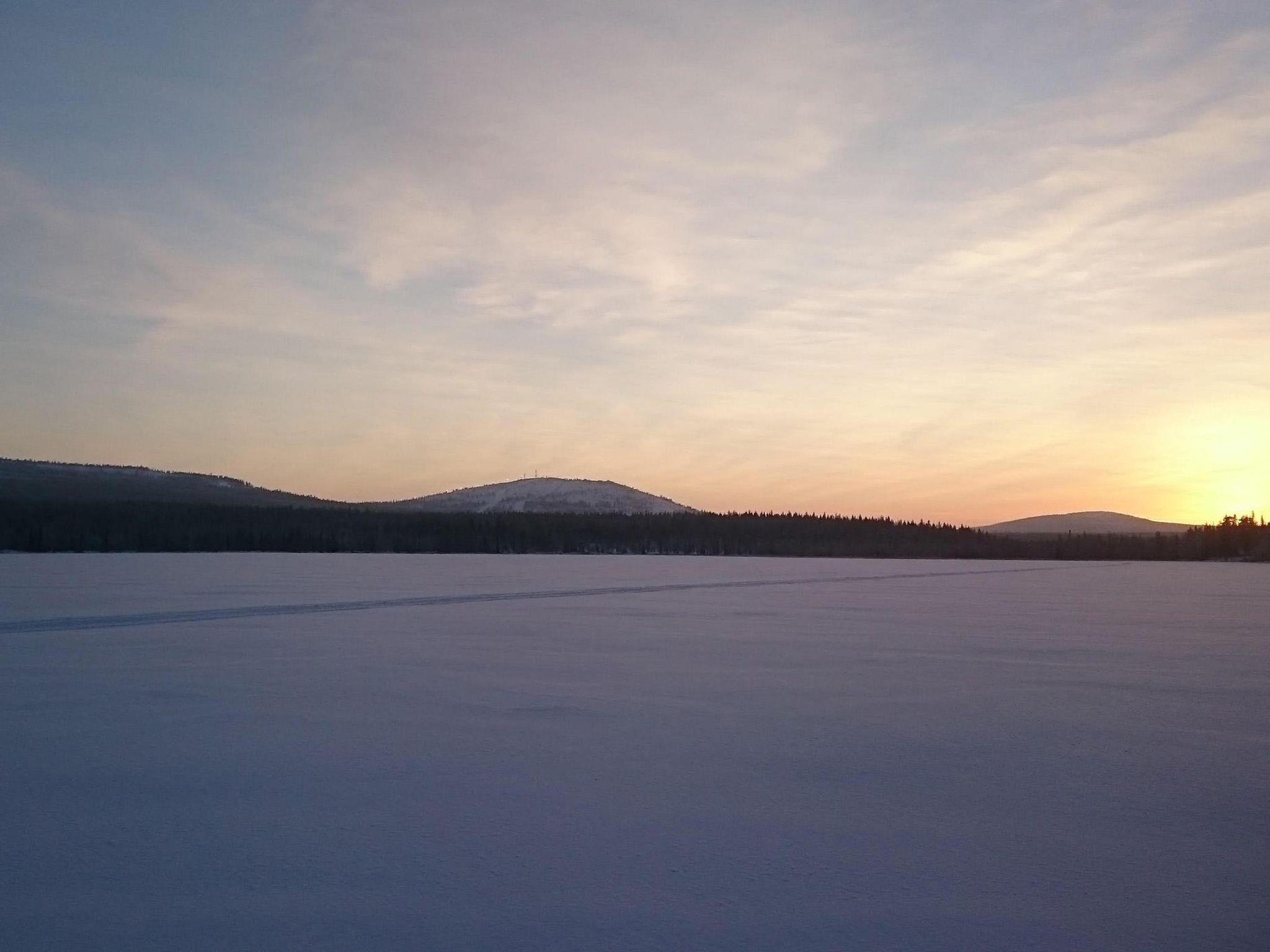 Eine flache, verschneite Landschaft mit fernen Hügeln und wolkenlosem Himmel.