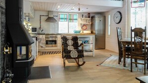 A cozy kitchen with a stove, oven, and refrigerator. There is a dining table with chairs and a rocking chair. A loft area is visible above the kitchen. - Teppolan rinne by Interhome (Salla)
