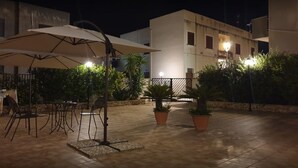 Ein Patio mit Tischen und Stühlen, Blumentöpfen und einem Gebäude im Hintergrund.