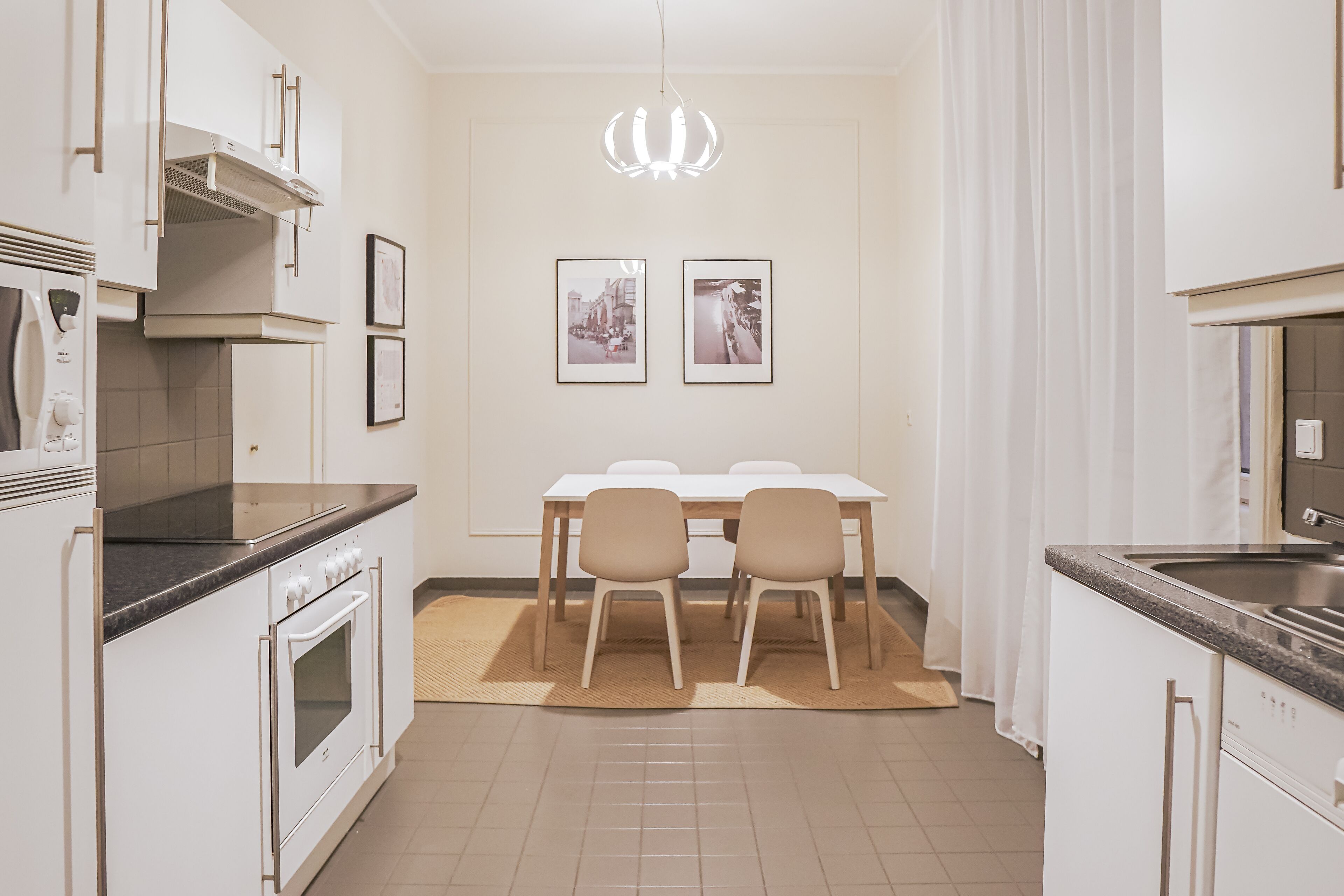 Een moderne keuken met witte kasten, een inbouwoven en een eethoek met een tafel en stoelen.