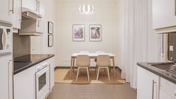 Een moderne keuken met witte kasten, een inbouwoven en een eethoek met een tafel en stoelen.