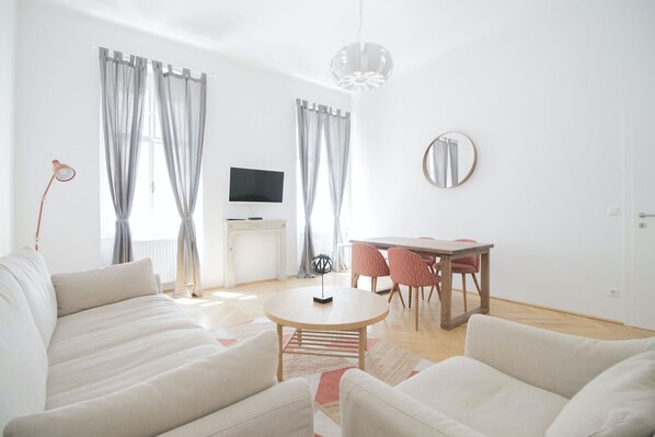 A modern living room with a sofa, a round coffee table, and a dining area with chairs and a table. - HeyMi Apartments Stephansdom (Vienna)