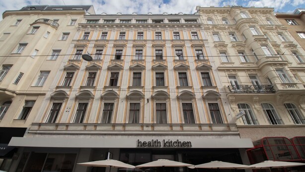Ein Gebäude mit einem 'Health Kitchen'-Schild, großen Fenstern und klassischer Architektur.