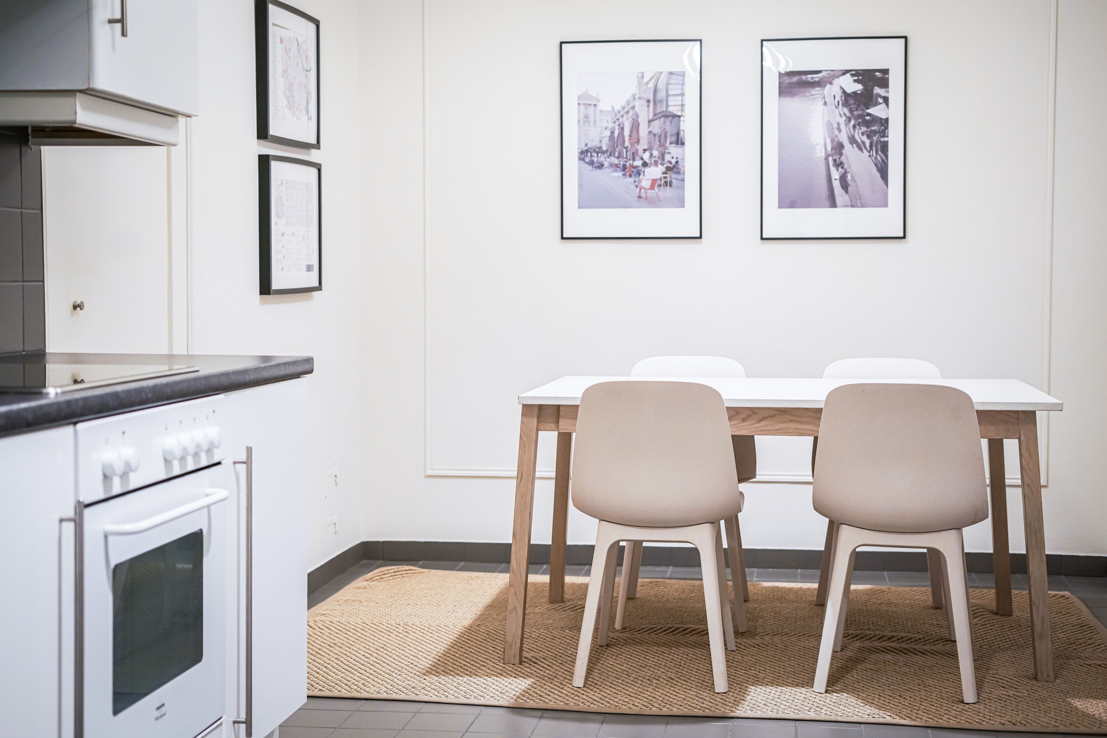 A modern kitchen with white cabinetry, a built-in oven, and a dining area with a white table and two chairs.