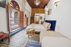 A room with a bed, a small table, a bench, a patterned floor, and a decorative door.