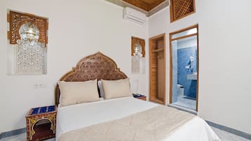 Un dormitorio con una cama grande, cabecera de madera, paneles decorativos en la pared, una mesita de noche y vista al baño.