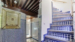 Una escalera con baldosas de diseño azul y blanco, una pared decorativa con motivos geométricos y un techo con vigas de madera.