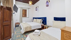 Habitación de hotel con dos camas, televisión, armario de madera, suelo estampado e iluminación decorativa en la pared.