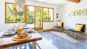 Una cocina luminosa con una mesa de comedor dispuesta para el desayuno, ventanas amplias, sillas de mimbre y techo de madera.