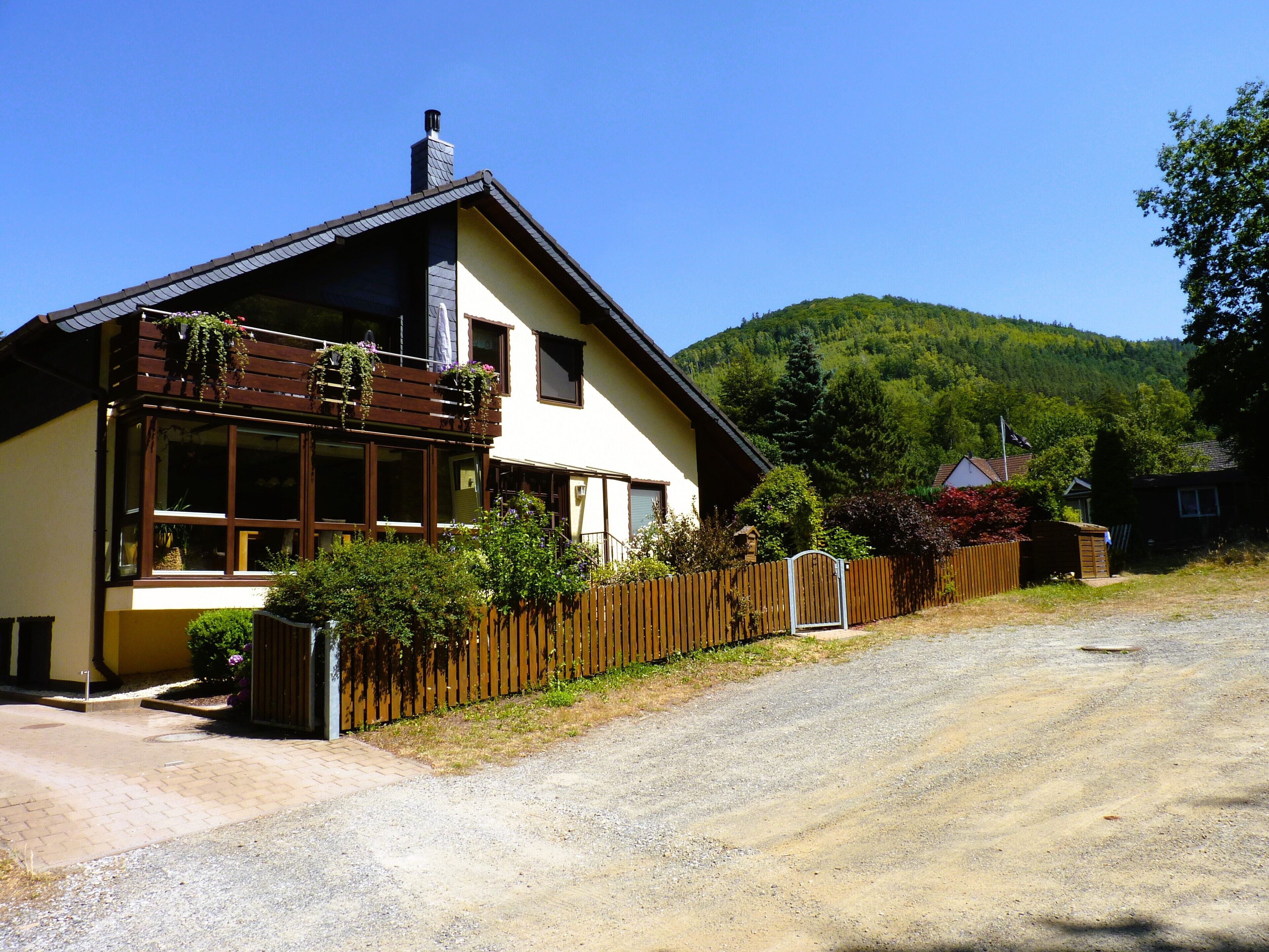 Uma casa de dois andares com varanda, entrada de cascalho e cerca de madeira.