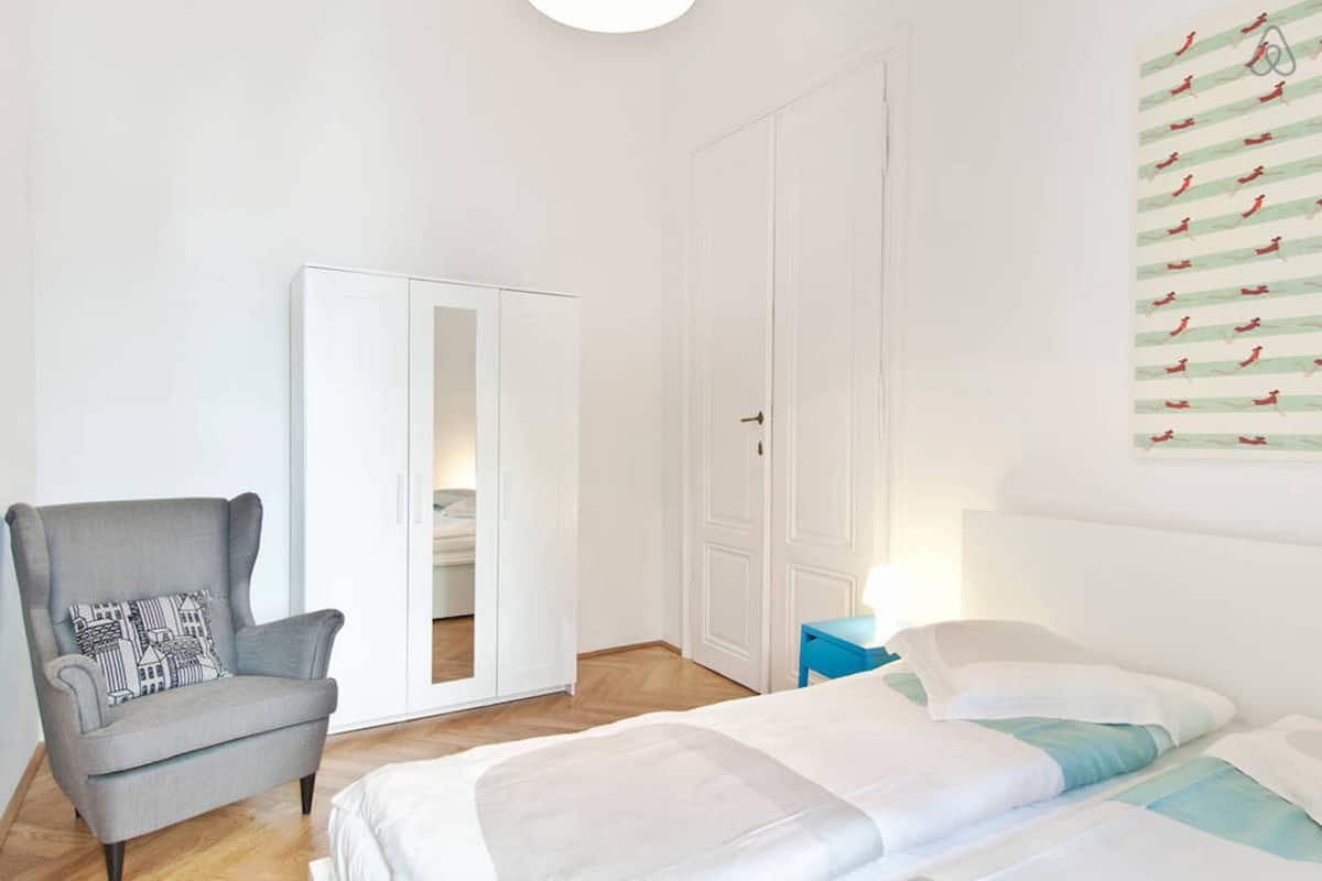 A bedroom with a bed, a chair, a wardrobe, and a wall with a pattern.