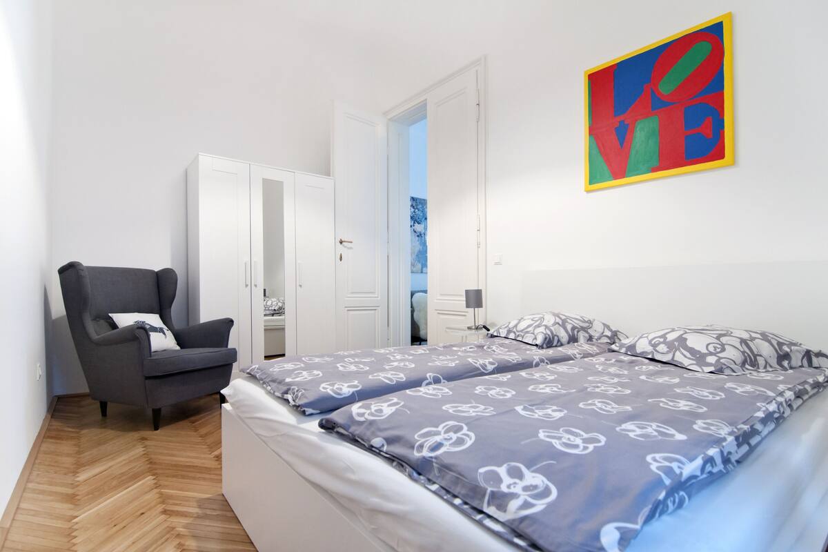 A bedroom with a bed, a chair, a wardrobe, and a painting on the wall.