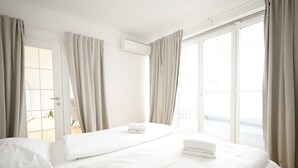 Habitación de hotel con dos camas, una puerta corrediza al balcón y un equipo de aire acondicionado blanco en la pared.