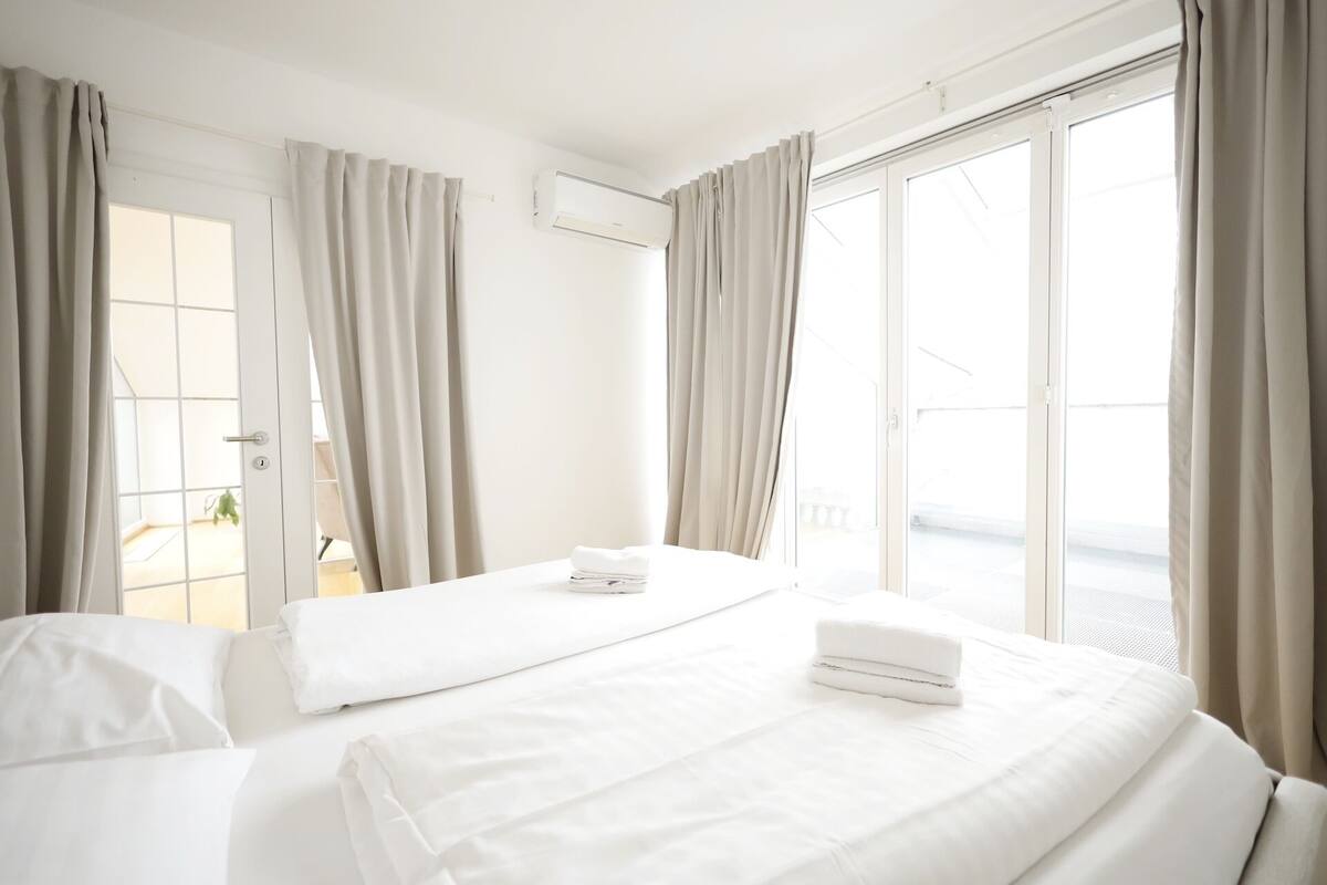 A hotel room with two beds, a sliding glass door to the balcony, and a white air conditioning unit on the wall.