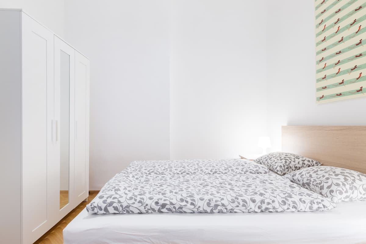 A bedroom with a bed, a wooden headboard, a white wardrobe, and a wall with a striped pattern.