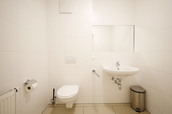 A small, clean bathroom with a toilet, sink, and trash can. - HeyMi Apartments Oper (Vienna)