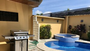 Un patio trasero con un porche de piedra, una piscina, un jacuzzi y una parrilla.