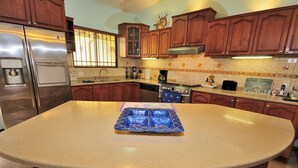 Una cocina con armarios de madera, un refrigerador de acero inoxidable, un horno empotrado y una isla grande con una bandeja azul.