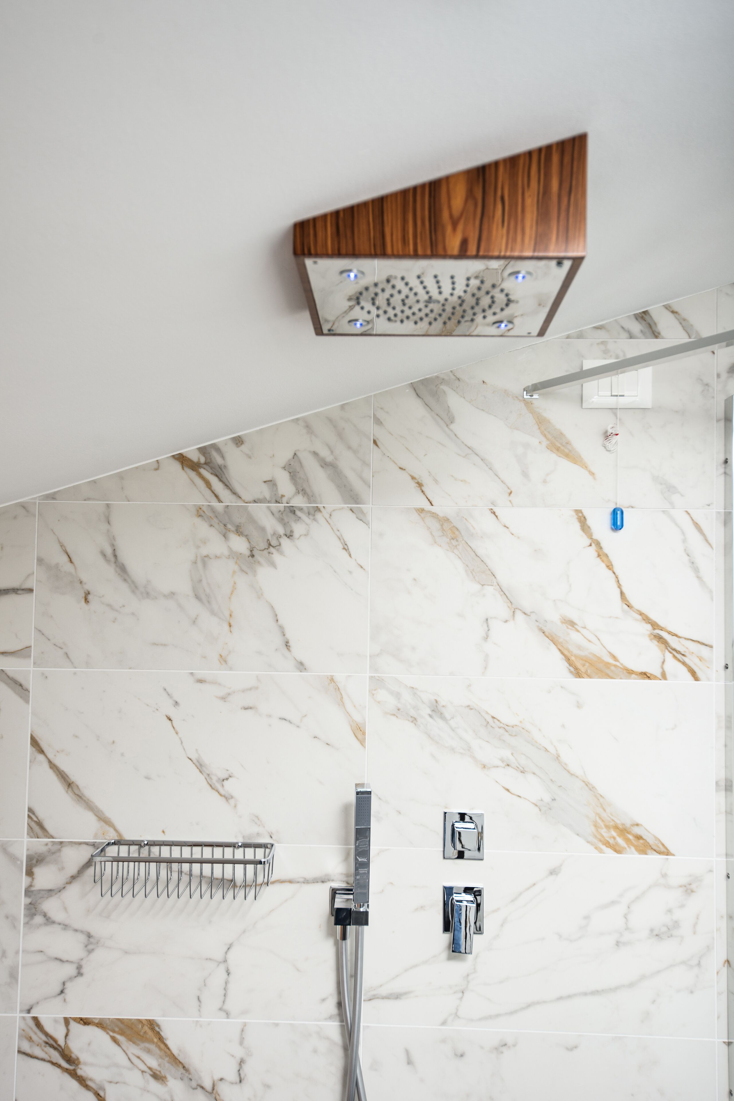 A bathroom with a shower, marble tiles, a wooden shelf, and a metal towel rack.