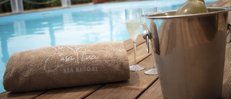 Zona de piscina en un complejo turístico con spa, una botella de champán, vasos y una toalla.